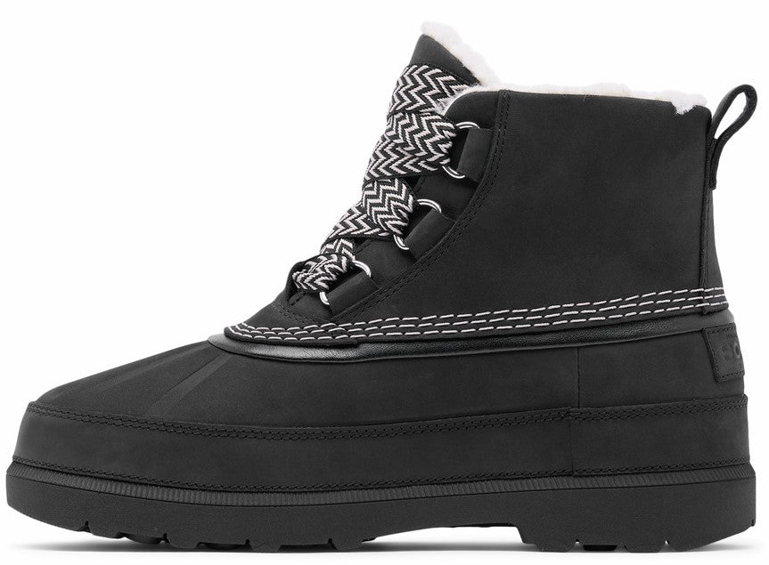 A black lace-up winter duck boot with a white faux-fur collar, a thick rubber sole, and a patterned black-and-white zigzag lace, viewed from the side.