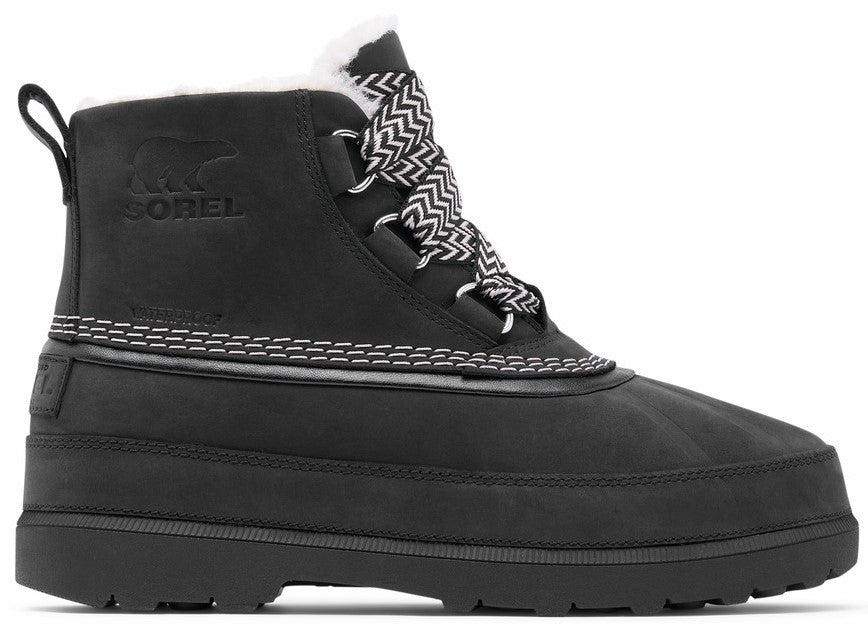 A black waterproof boot with a white fuzzy collar, featuring zigzag pattern laces, visible contrast stitching along the middle, a thick lug sole, and a debossed bear logo on the side.