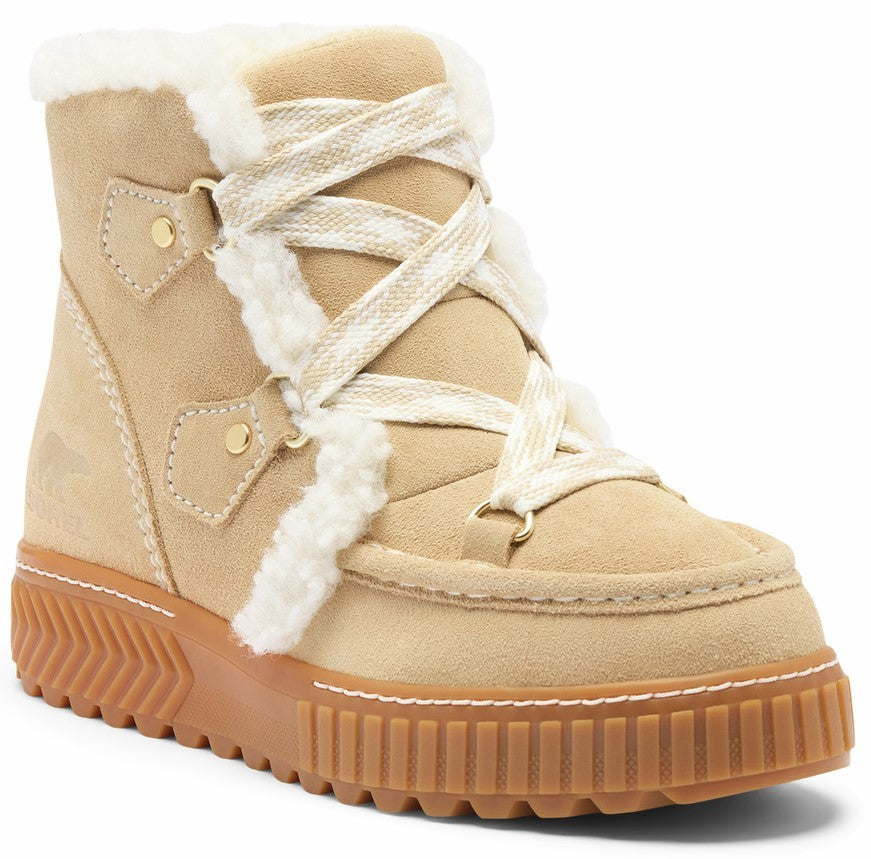 A tan suede winter boot with white faux-fur trim, white crisscross laces, gold-toned metal hardware, and a thick, textured brown rubber sole.