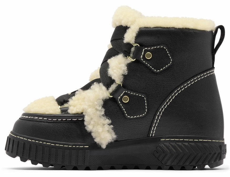 A black ankle boot with white sherpa trim, a thick black lug sole, white contrast stitching, and two brass-toned eyelets on each side for the lacing system.