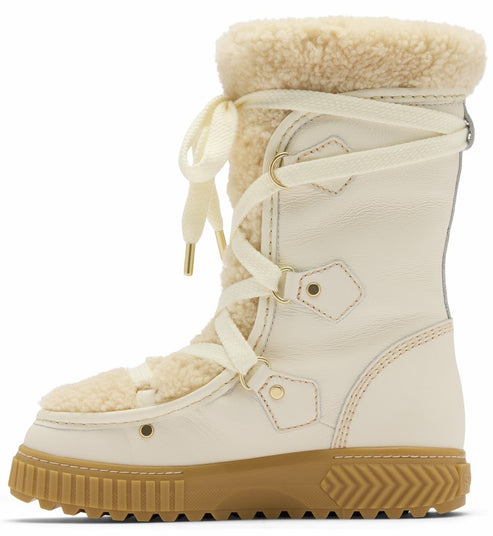A cream-colored leather snow boot with tan shearling lining and trim, featuring a wrap-around lace-up closure with gold hardware and a thick, textured tan rubber lug sole.