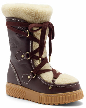 A brown leather mid-calf winter boot with a thick tan lug sole, featuring a cream-colored faux fur lining, brown lace-up front with gold-toned metal hardware, and the SOREL logo embossed on the side.