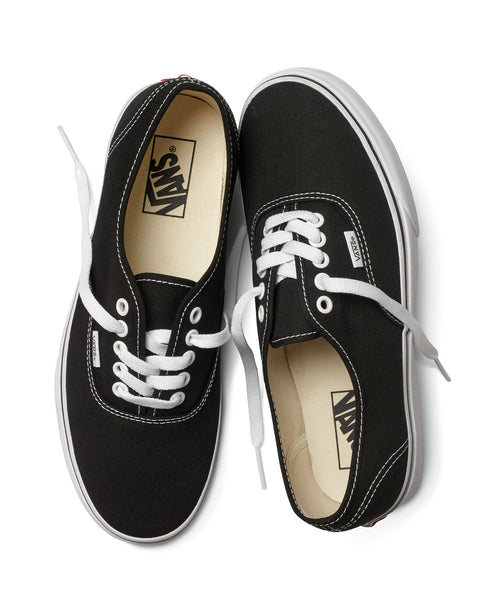 Two black canvas low top sneakers with white laces and white soles.