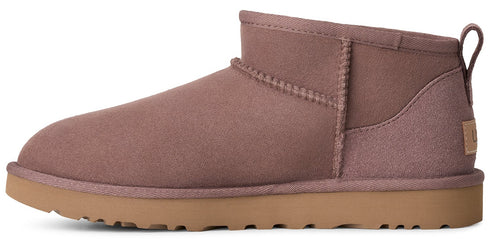 A side profile of a mauve, suede ankle boot with a flat, light tan rubber sole and a small branded tab on the heel.
