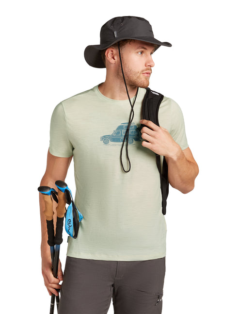 Man wearing a hat, a light green t-shirt with a car graphic, gray pants, holding trekking poles, and a black vest over the shoulder.