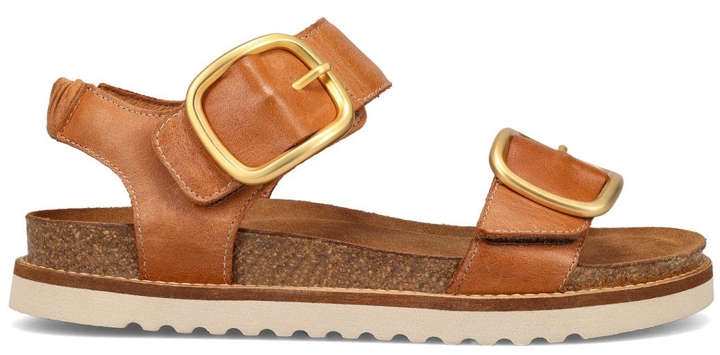A tan sandal with two straps, each with a large gold buckle.
