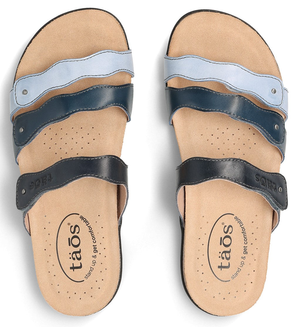 Two sandals with three straps each in light blue, dark blue, and black, with the word "taos" on the insole.