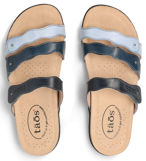 Two sandals with three straps each in light blue, dark blue, and black, with the word "taos" on the insole.