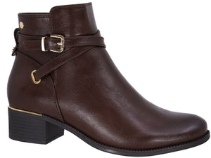 A dark brown leather ankle boot with a low block heel, featuring a decorative strap with a gold-tone buckle and a small gold metallic accent above the heel.