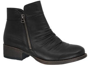 A black ankle boot with a low, block heel and a metallic side zipper detail, featuring slightly ruched leather on the front.