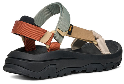 A sandal with thick black ridged sole and multiple tan, orange and green nylon straps.