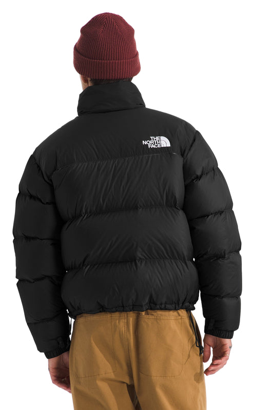 A person wears a black puffer jacket with a white logo on the back and a red beanie.