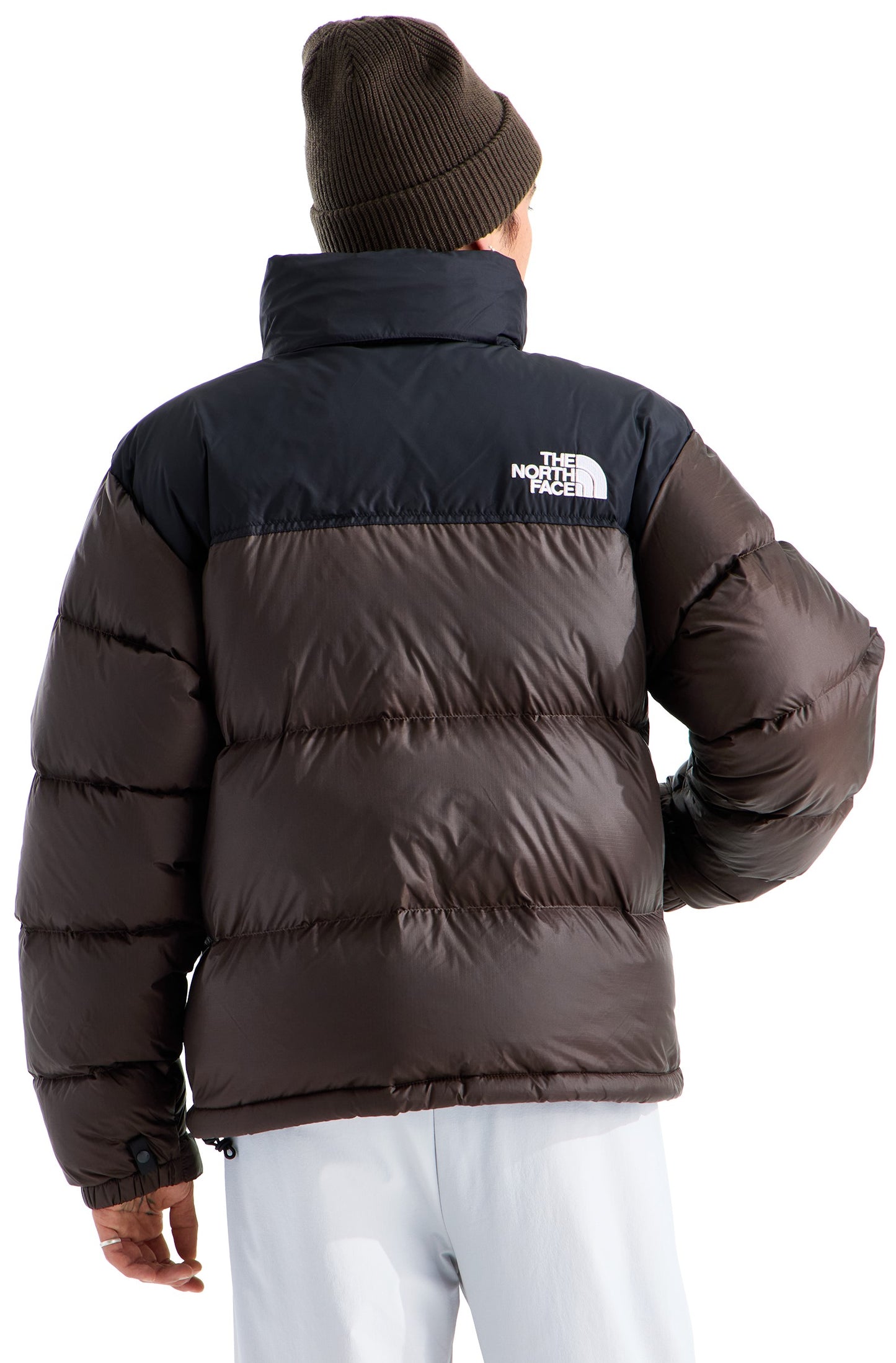 A person viewed from the back wearing a dark brown ribbed beanie and a dark brown puffer jacket with black shoulders and the logo "THE NORTH FACE" embroidered in white on the back right shoulder.