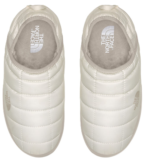 Overhead view of two white quilted slippers with logos visible on the insole and near the toe.