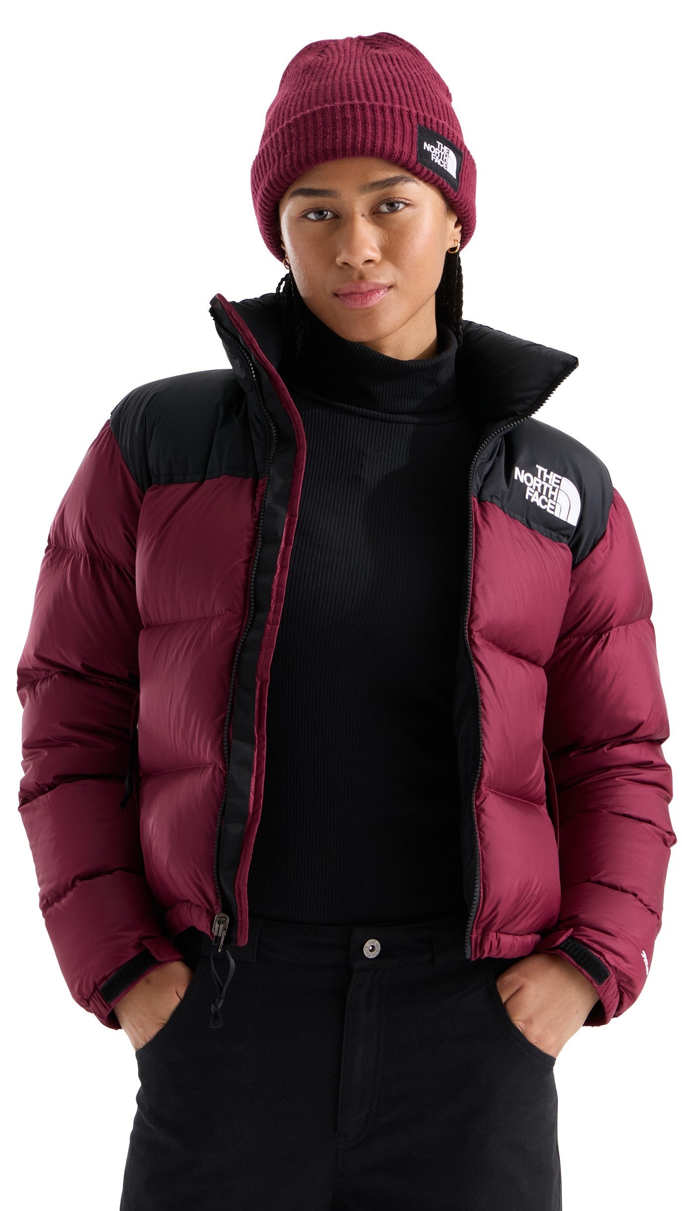 A person wearing a dark maroon beanie and a matching maroon and black puffer jacket with a black turtleneck underneath.