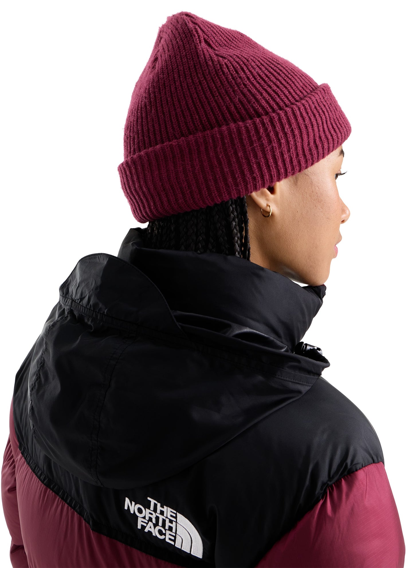 A person viewed from behind and the side wearing a magenta ribbed knit beanie and a black and magenta hooded puffer jacket with The North Face logo on the back.