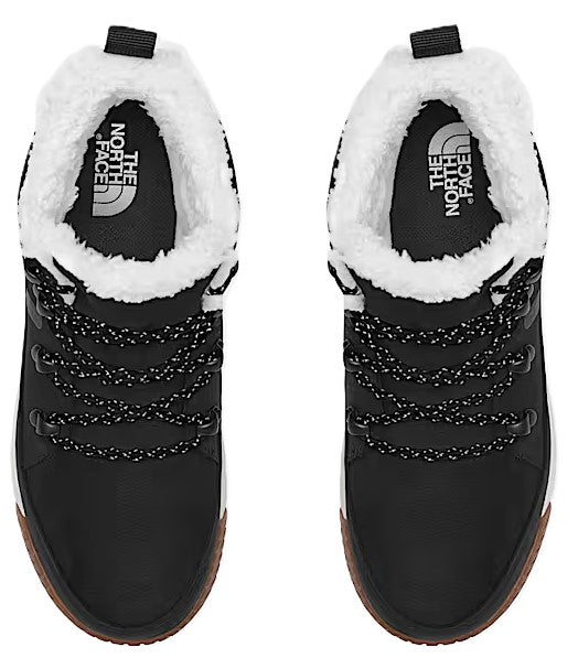 Overhead shot of a pair of black boots with white faux fur lining, black laces, and brown soles. The North Face logo is visible on the insole.