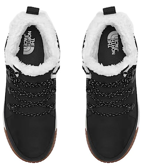 Overhead shot of a pair of black boots with white faux fur lining, black laces, and brown soles. The North Face logo is visible on the insole.