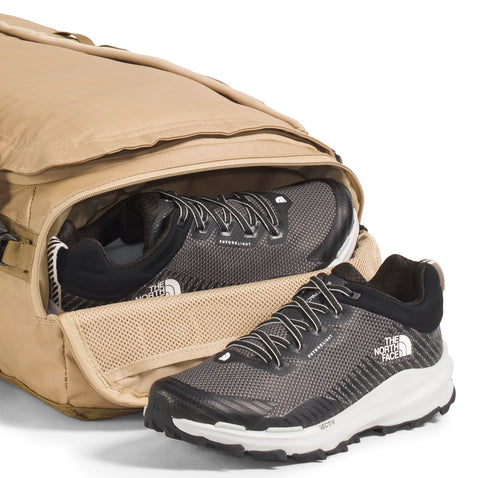 Tan duffel bag with one gray and black shoe inside and another one standing beside it.