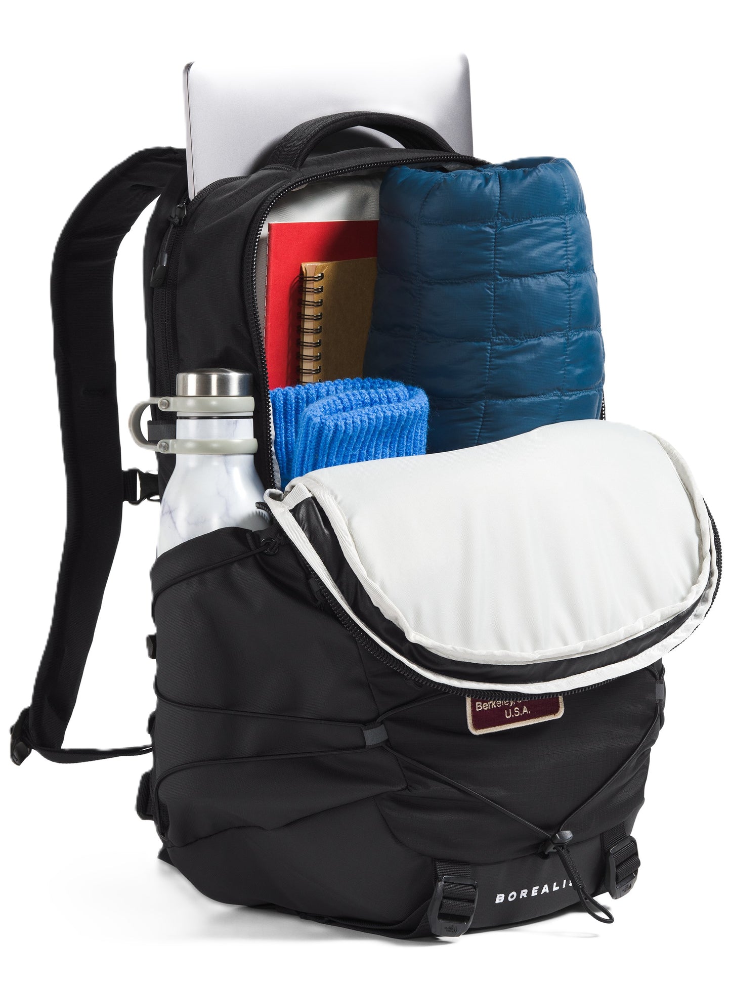 Open black backpack with water bottle in side pocket, laptop, notebooks, blue towel, and blue jacket inside.