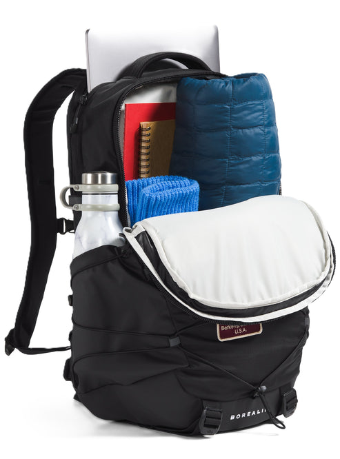 Open black backpack with water bottle in side pocket, laptop, notebooks, blue towel, and blue jacket inside.
