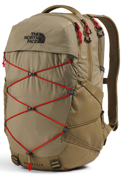 A tan The North Face Borealis backpack shown from a three-quarter angle, featuring a front bungee cord system with bright red cords, black hardware, black zippers with red pull tabs, and a top handle against a white background.