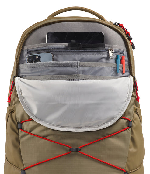 An open tan backpack with a grey interior featuring a top compartment for a tablet, a zippered pocket with a phone, two slots for pens, and a large open pouch, all accented with red zipper pulls and cord detailing on the front.