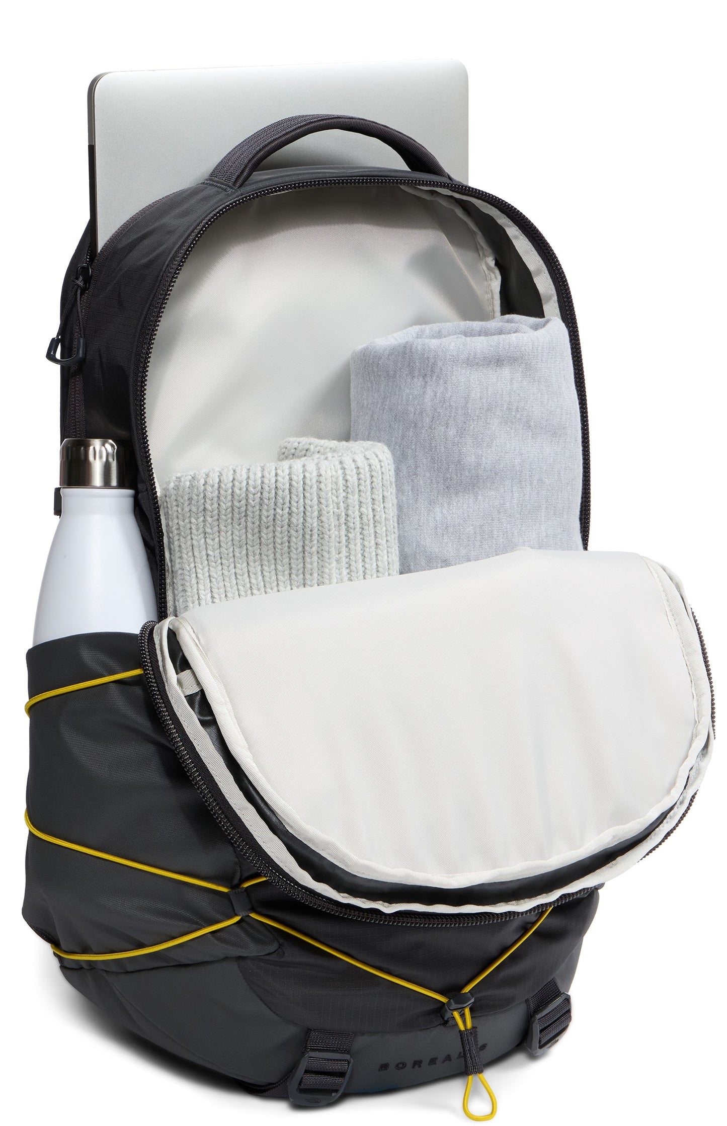 A black backpack with yellow bungee cords on the front, showing an open main compartment filled with folded light gray clothing, a laptop sleeve with a silver laptop inside, and a water bottle in the side pocket.
