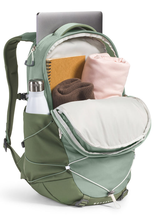 Open sage green backpack with laptop, notebook, bottle, beanie and sweater inside.