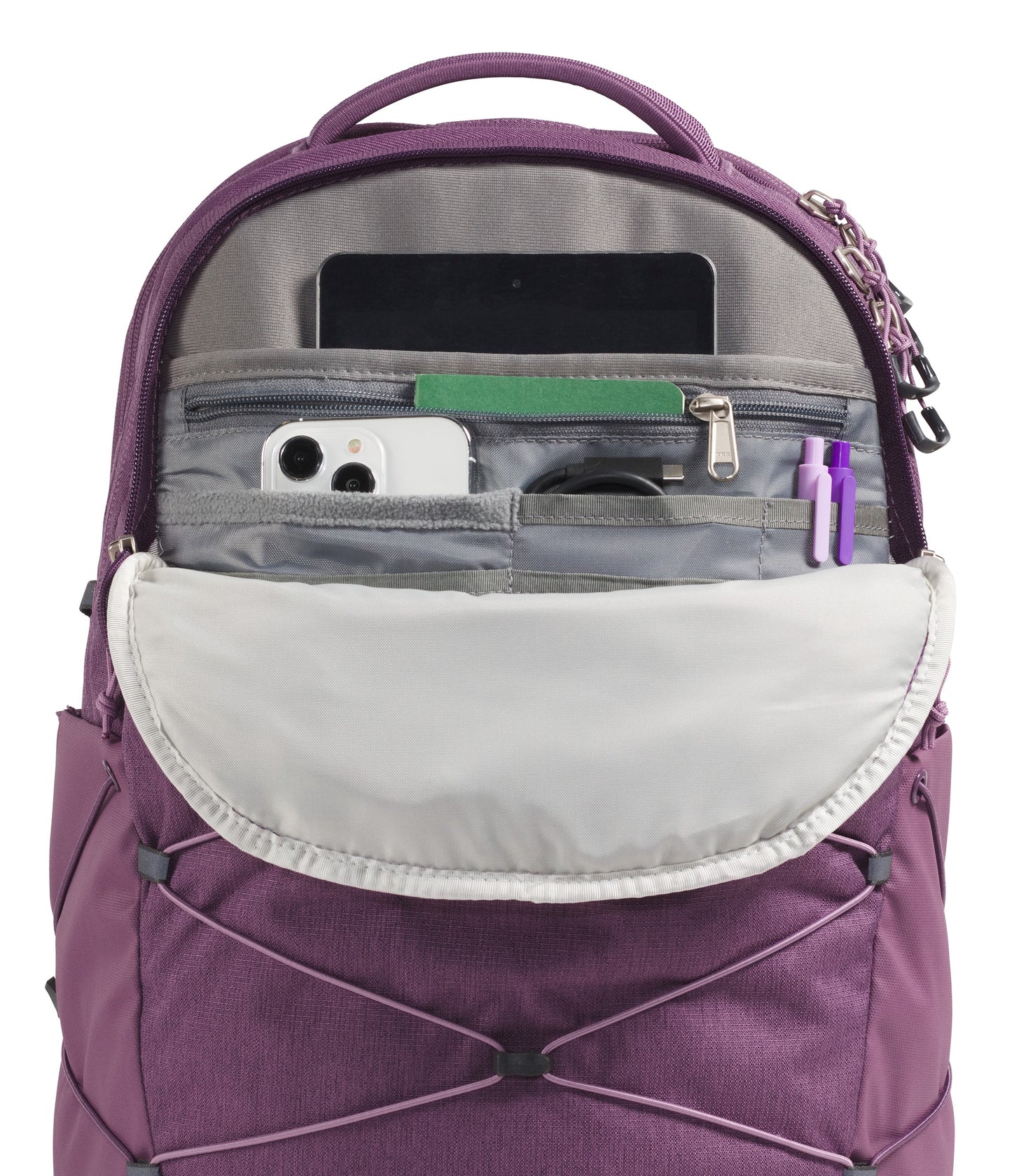 A close-up of a purple backpack's open front organizer pocket showing a tablet in a sleeve, a white smartphone, a zipper pocket, a cable, and two pens inside, with an external bungee cord system on the exterior.