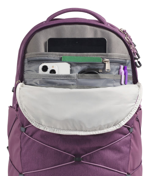 A close-up of a purple backpack's open front organizer pocket showing a tablet in a sleeve, a white smartphone, a zipper pocket, a cable, and two pens inside, with an external bungee cord system on the exterior.