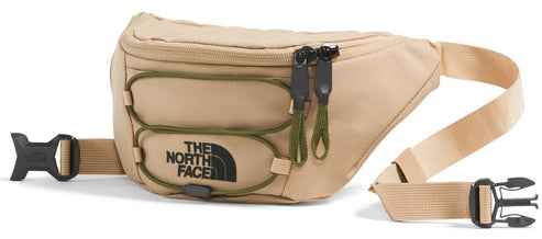 A tan waist bag featuring an external olive green cord system and black zipper pulls, with the black text "THE NORTH FACE" logo printed on the front, attached to a matching tan adjustable strap with a black plastic buckle.