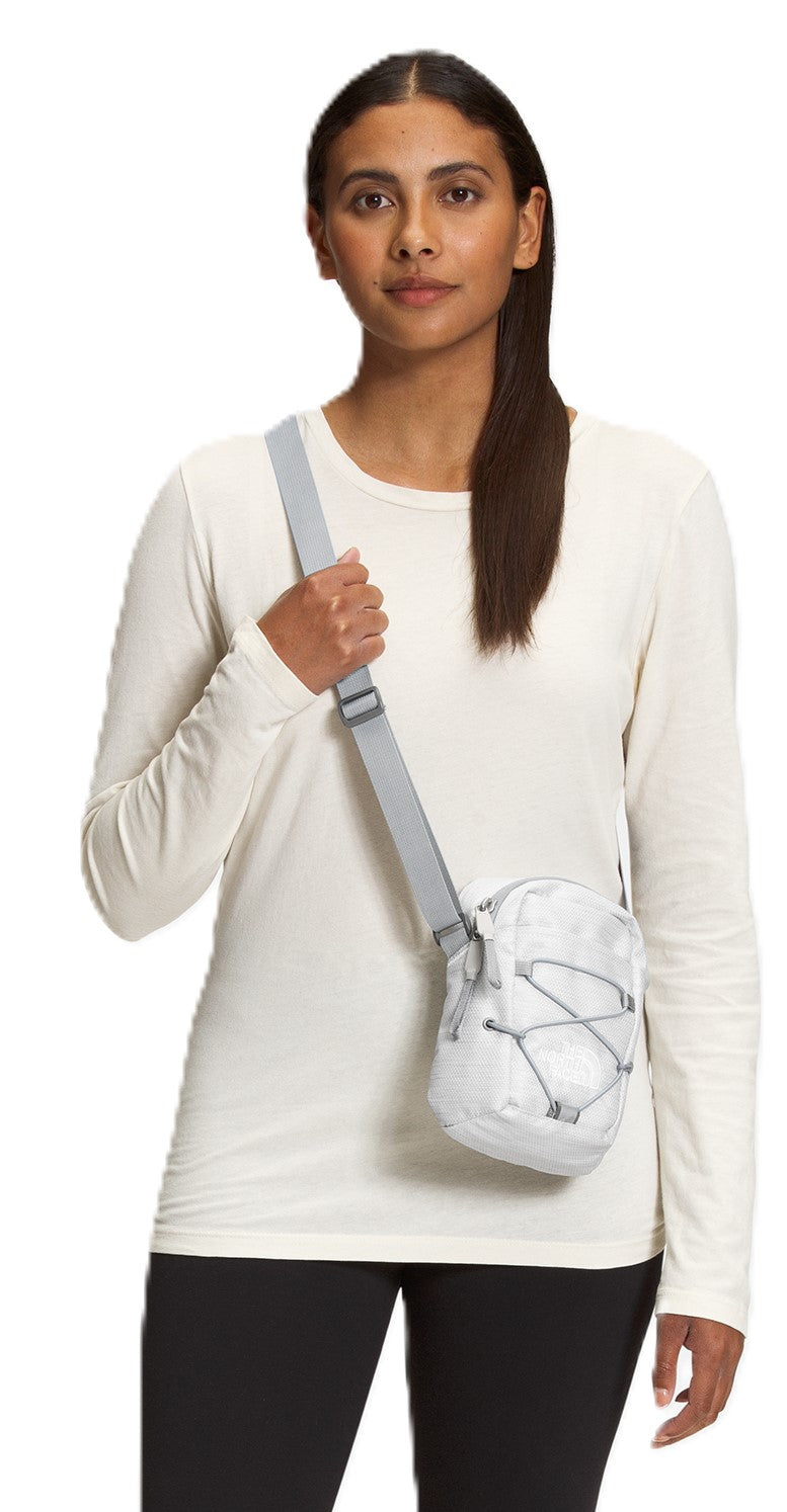 A person models a small white crossbody bag with gray bungee cords and a gray strap over their shoulder.