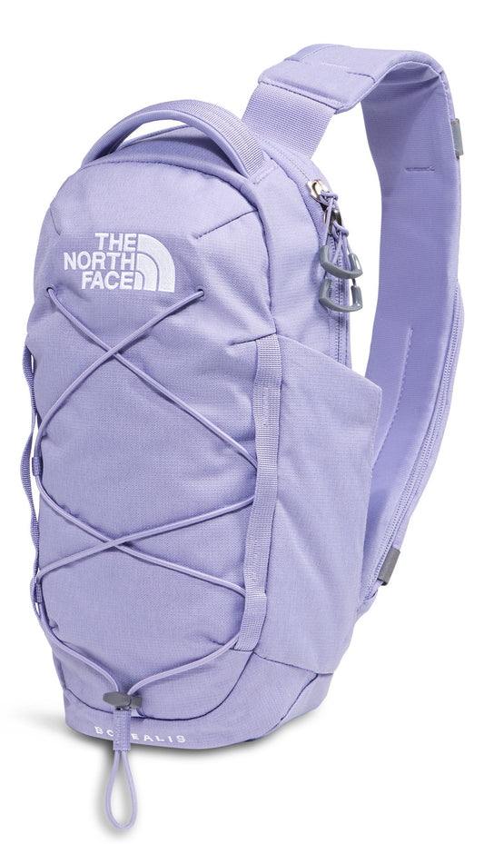 A light purple, single-strap sling backpack with a prominent top handle, a zippered main compartment, a crisscross bungee cord system on the front, and the brand name The North Face visible on the upper front.