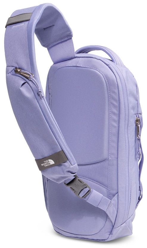 A light purple, single-strap sling backpack shown from the back, featuring a padded back panel, a single adjustable shoulder strap with a zipper pocket and The North Face logo, and a side zipper closure.