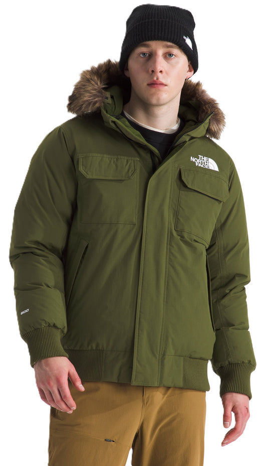 A man wearing a black beanie and olive green winter jacket with a fur-trimmed hood and khaki pants.