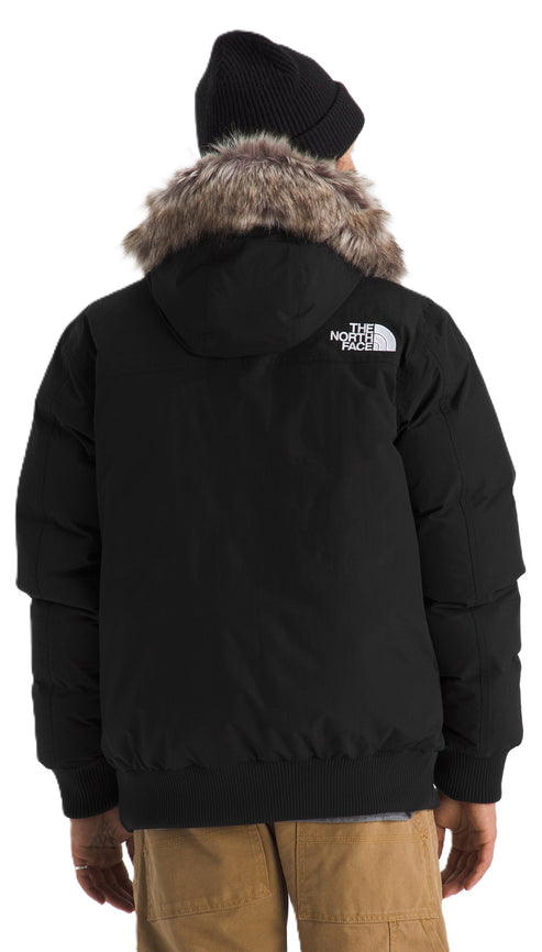 Back view of a person wearing a black hooded down jacket with faux fur trim and a black beanie.