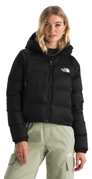 A woman wearing a black cropped hooded puffer jacket with a white logo on the chest and light green cargo pants with a small white logo on the pocket.