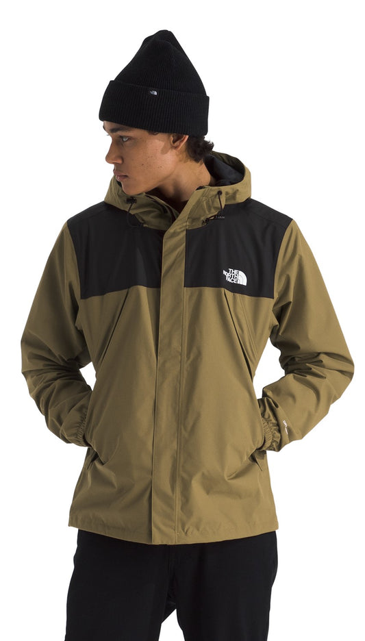 A person wears a khaki and black hooded jacket with a white logo on the left chest.