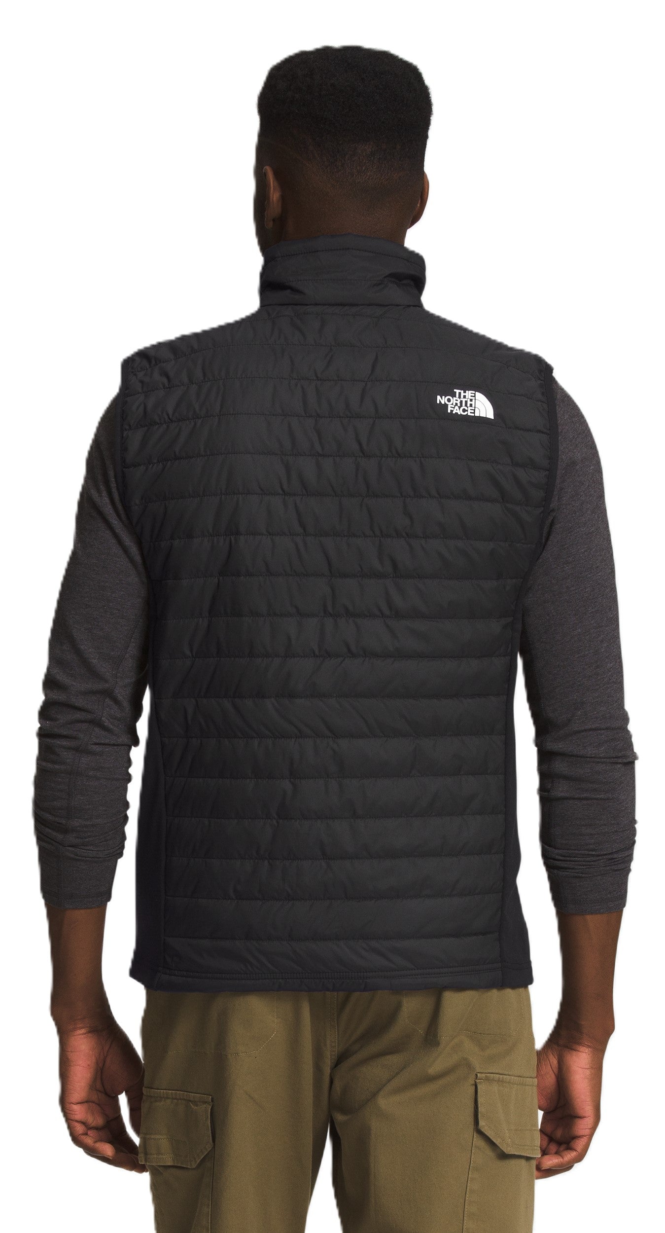 A person is shown from the back wearing a black quilted vest with a white logo on the right shoulder.