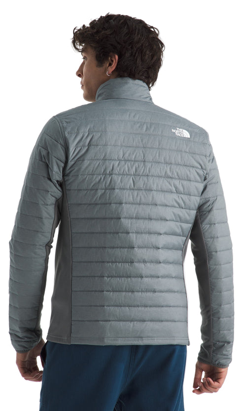 Back view of a man wearing a gray quilted jacket with a visible white logo near the shoulder.