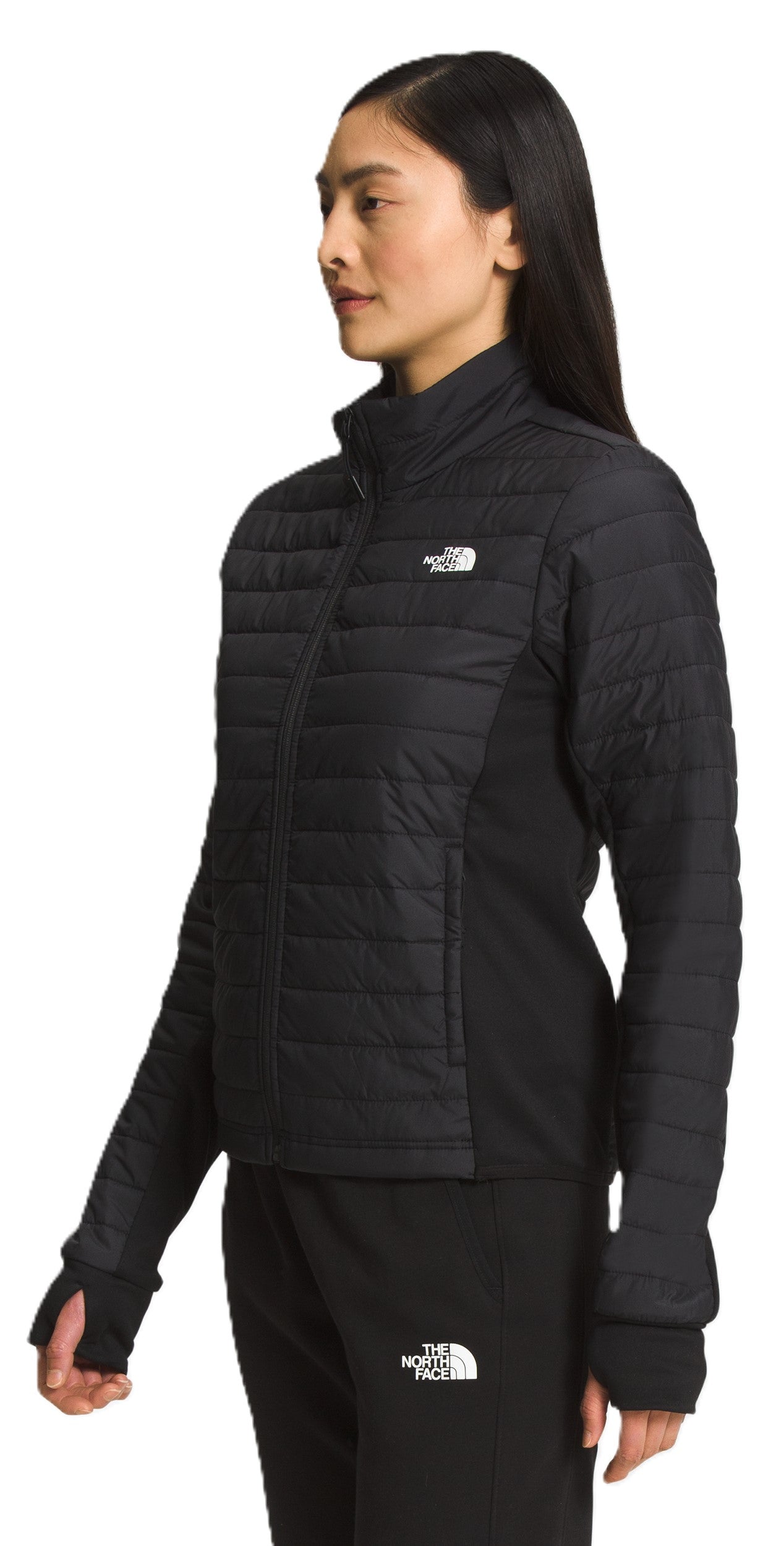 A woman wearing a black quilted jacket and black pants, with a white logo on both.