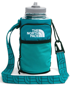 A teal, cylindrical water bottle carrier with an adjustable shoulder strap featuring a repeating logo pattern, a carabiner attachment on the side, and a clear water bottle with a grey lid inside it, with 'THE NORTH FACE' and its logo printed in white on the front pocket.