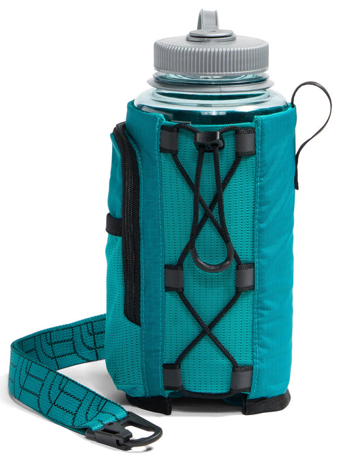A teal water bottle holder with an adjustable bungee cord system on the front, a side zipper pocket, and a matching patterned carry strap with a black plastic clip, holding a clear water bottle with a grey cap.