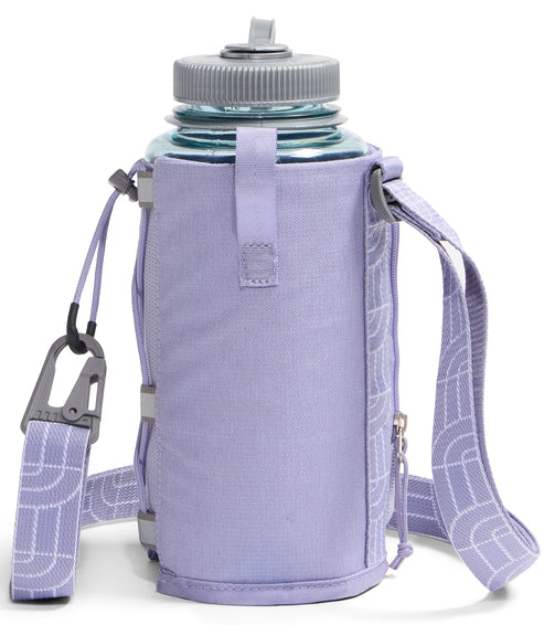 A light purple, cylindrical insulated bottle sleeve with a matching adjustable shoulder strap featuring a white geometric pattern. The sleeve has a side zipper, a gray carabiner attached to a cord on the left, and holds a clear water bottle with a gray screw-top cap.