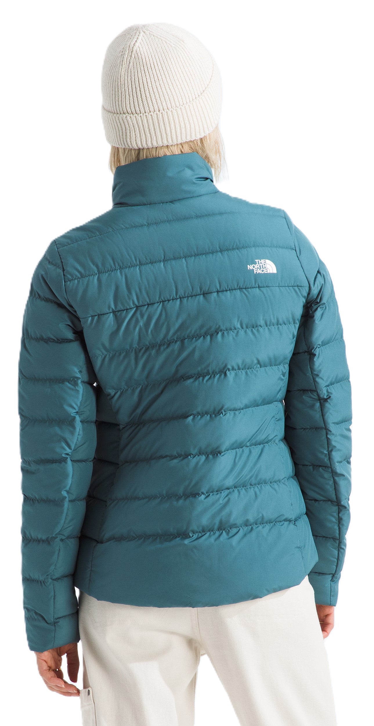 A woman wearing a teal puffer jacket and white beanie, back view.