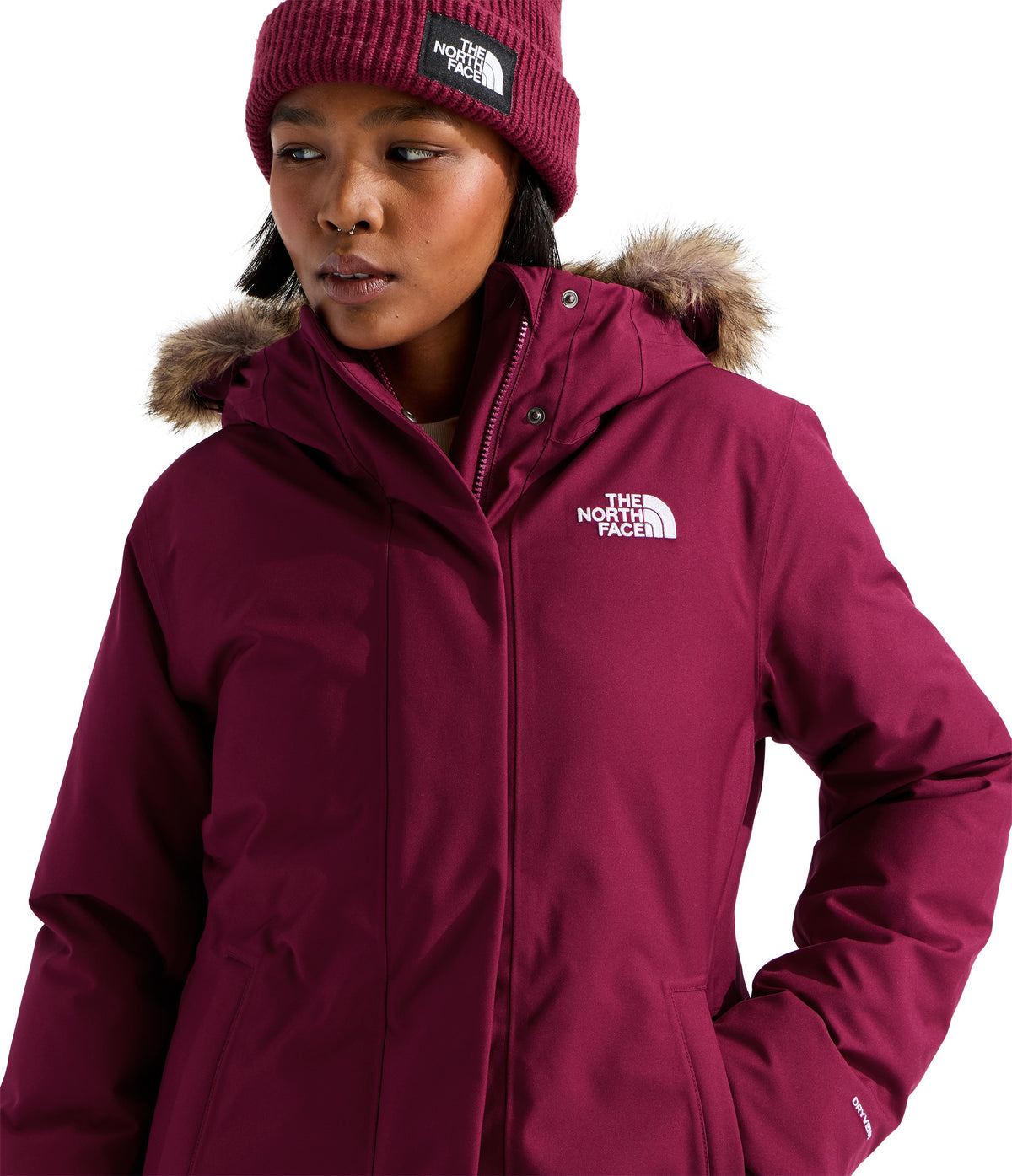 A person wearing a dark magenta winter parka with a faux-fur trimmed hood and a matching beanie with the text "THE NORTH FACE" visible on both.