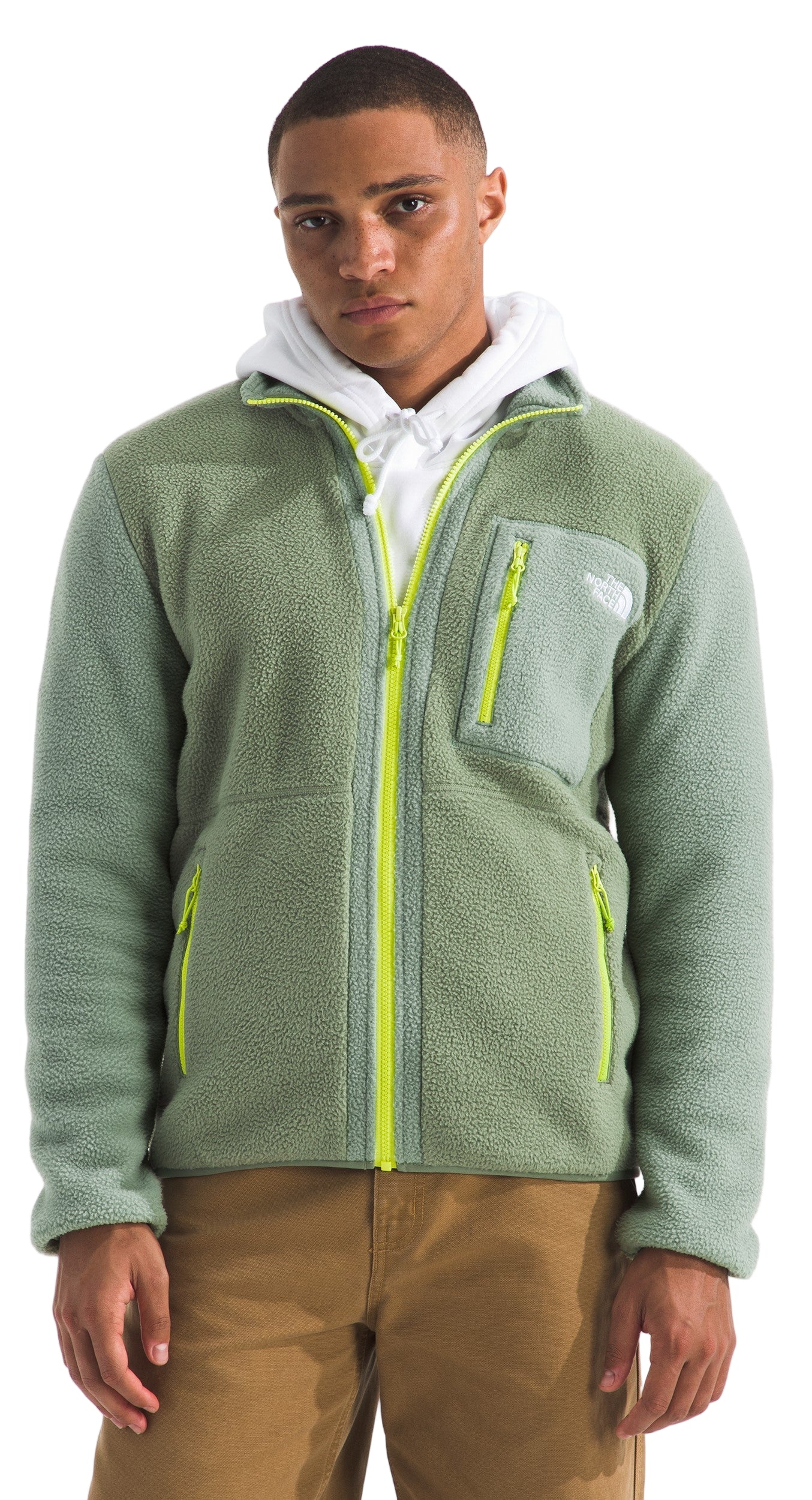 A man wearing a light green fleece zip-up jacket with yellow zipper and khaki pants.