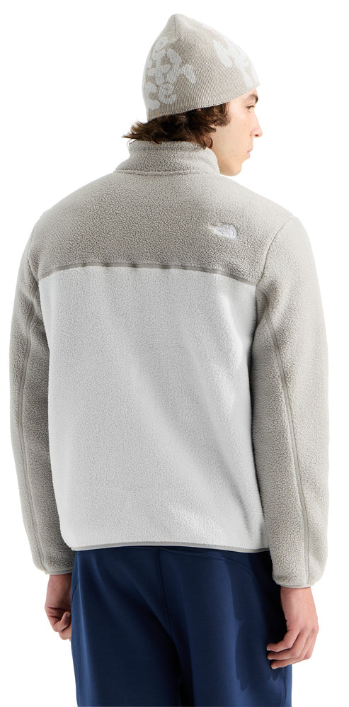 A back view of a person wearing a light grey, fuzzy-textured jacket with a mock neck collar and a matching beanie featuring large white text, paired with dark blue shorts.