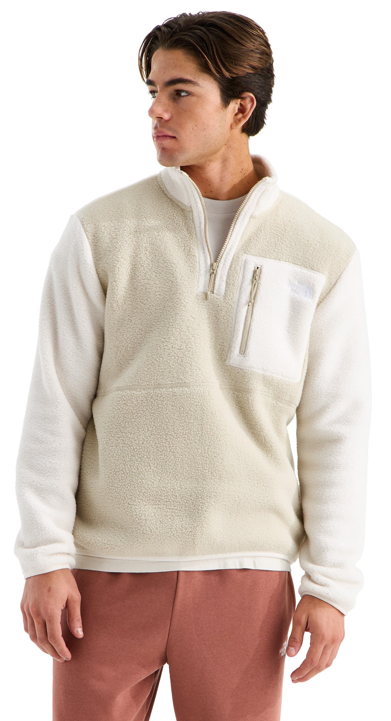 A man wearing a cream-colored, long-sleeved, quarter-zip fleece pullover with a textured, fuzzy body, smooth white sleeves, and a vertical zippered chest pocket, paired with terracotta-colored pants.